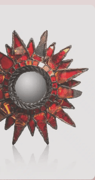 “Espejo decorativo en forma de sol con fragmentos de vidrio tintado rojo y marco de metal negro”